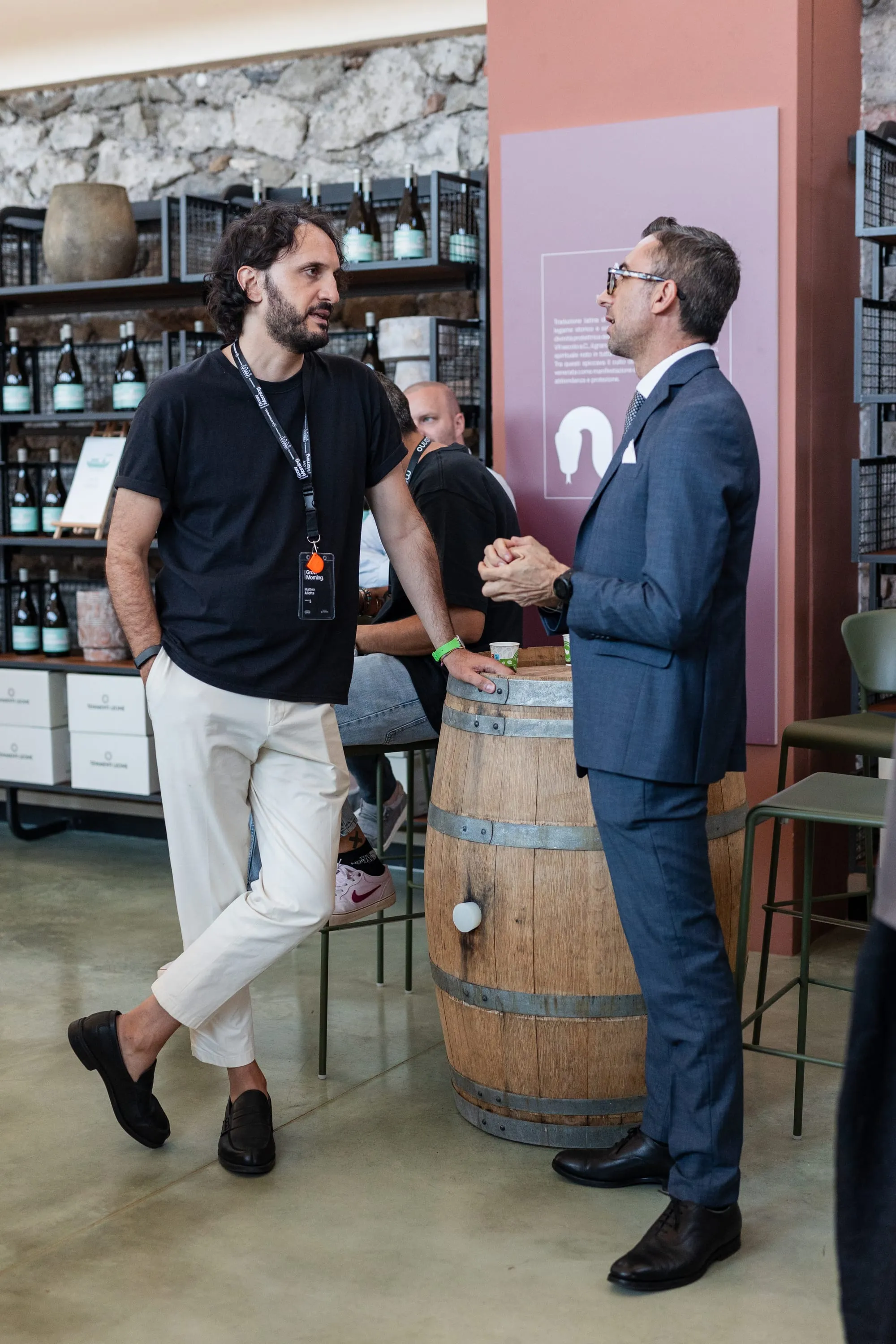 Due partecipanti si stringono la mano durante il networking, accanto alle botti della cantina.